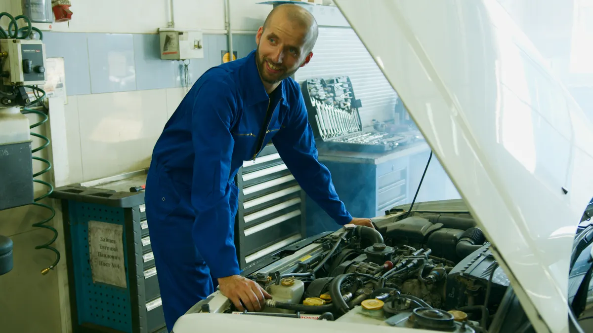 Auto technician in coveralls inspecting a car engine in a service bay