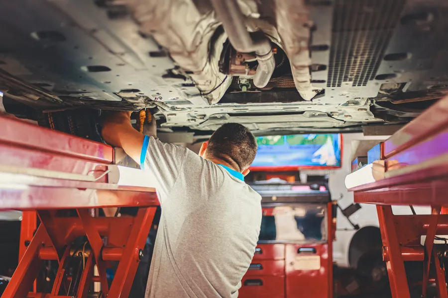 Technician inspecting the underside of a car raised on a two-post lift