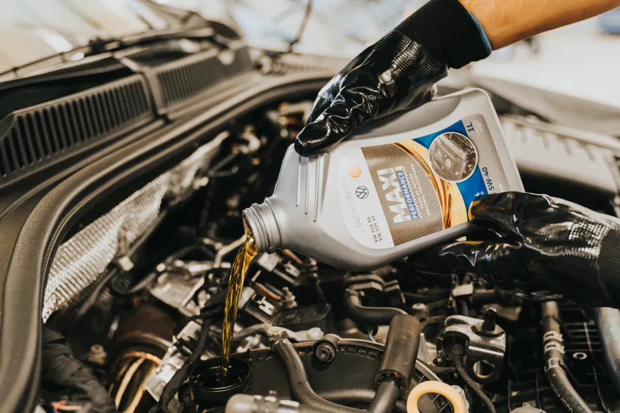 Gloved hands pouring fresh engine oil into a car engine during an oil change