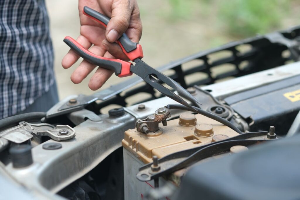 Hands using pliers on a car battery terminal