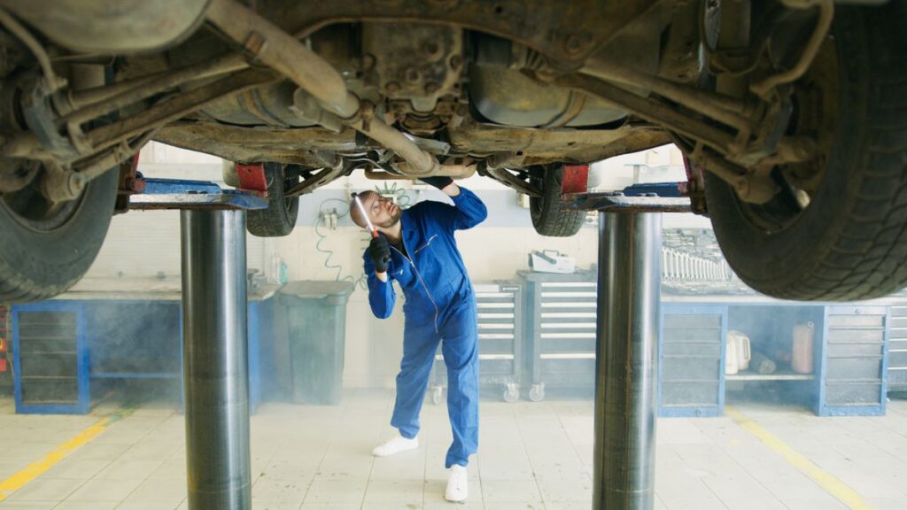 Mechanic inspecting the exhaust under a car on a lift