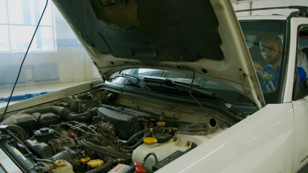 Mechanic checking a car engine under an open hood in a garage