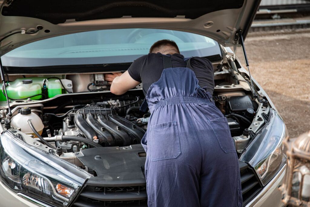 Mechanic leaning into an open engine bay to inspect the engine