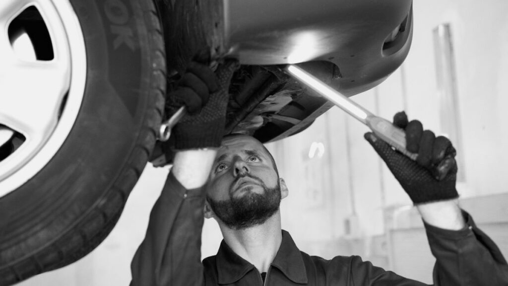 Mechanic inspecting a car's underbody in a workshop
