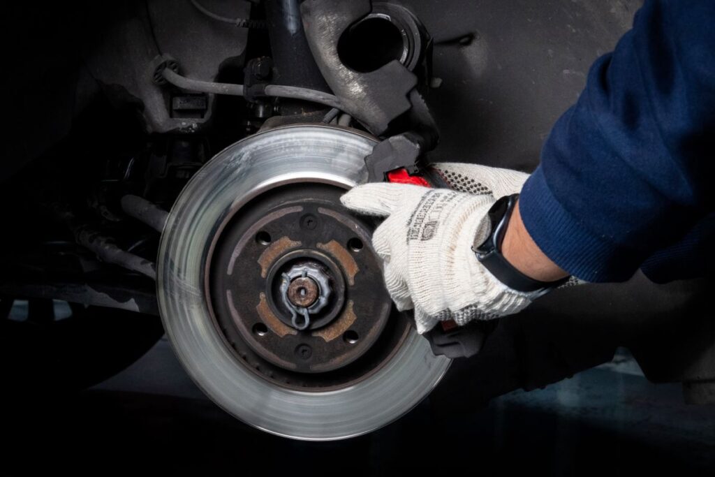 Gloved mechanic checking a brake rotor with the wheel removed