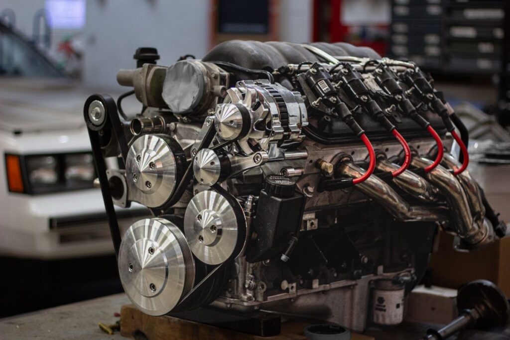V8 engine on a stand with its front belt pulleys exposed in a workshop